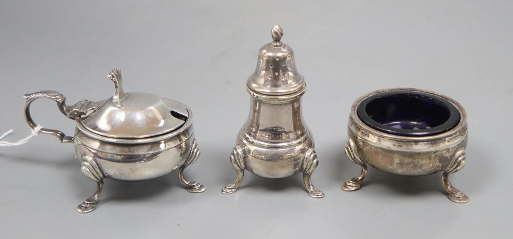 A silver three piece cruet set, with embossed girdle, on three hoof feet, blue glass liners, comprising a mustard pot, a salt and a pep